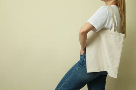 Young woman in blank t-shirt with bag against beige backgroundの写真素材