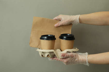 Hands in gloves hold paper cups and bag on gray backgroundの写真素材