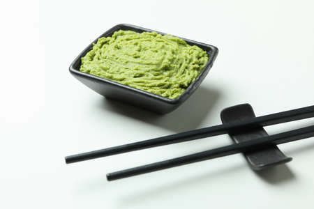 Chopsticks and wasabi sauce on white background