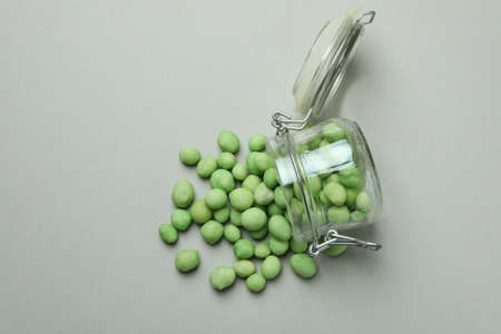 Glass jar with wasabi nuts on gray background