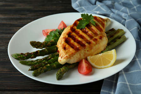 Plate with grilled chicken and ingredient on wooden background