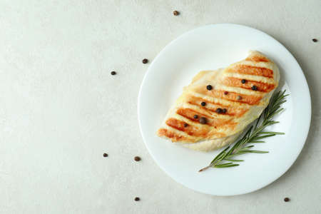 Plate with grilled chicken breast on white textured tableの写真素材