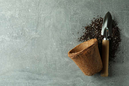 Coconut pot, gardening shovel and soil on gray textured background