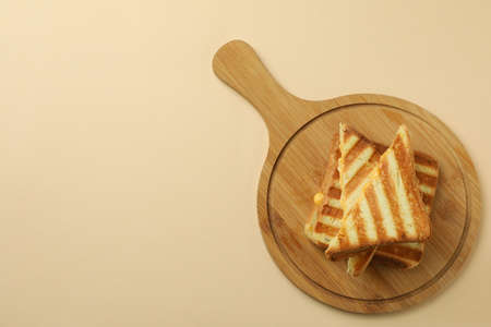 Board with grilled sandwiches on beige background