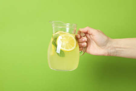 Female hand holds jug with lemonade on green backgroundの写真素材