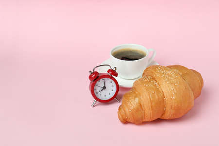 Croissant, coffee and alarm clock on pink background