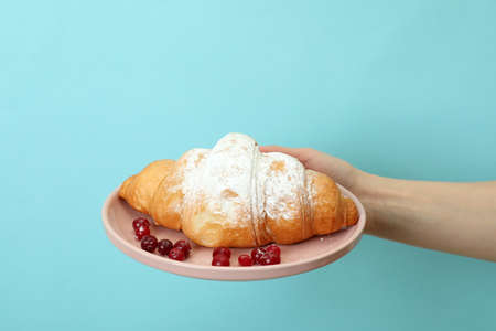 Female hand holds plate with croissant on blue background