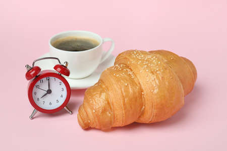 Croissant, coffee and alarm clock on pink backgroundの写真素材
