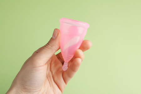 Female hand holds menstrual cup on green backgroundの写真素材