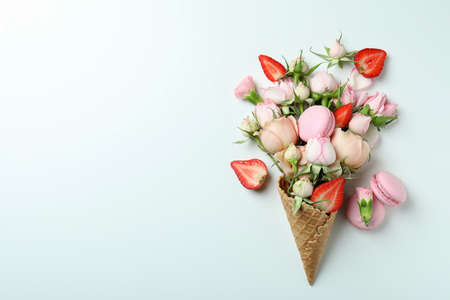Waffle cone with flowers, strawberry and macaroons on white backgroundの写真素材