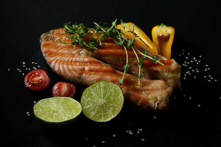Tasty grilled salmon and ingredients on black background