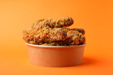 Bucket with fried chicken on orange background
