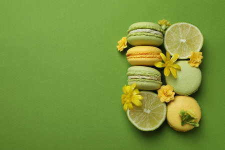 Macaroons, limes and flowers on green background