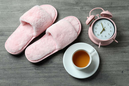 Alarm clock, slippers and tea on gray backgroundの写真素材