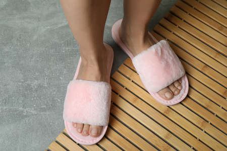 Female legs in pink slippers on bamboo on gray textured floor