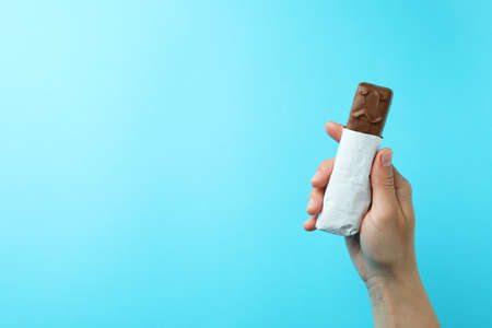 Female hand holds tasty candy bar on blue backgroundの写真素材