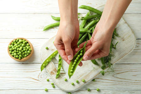 Female hands hold green pea on white wooden backgroundの写真素材