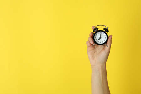 Female hand holds alarm clock on yellow backgroundの写真素材