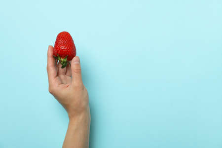 Female hand holds fresh strawberry on blue backgroundの写真素材