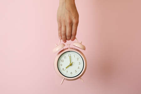Female hand holds alarm clock on pink background