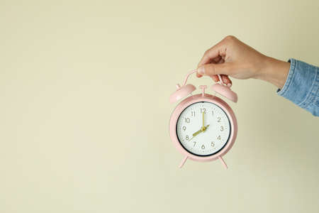 Female hand holds alarm clock on beige backgroundの写真素材