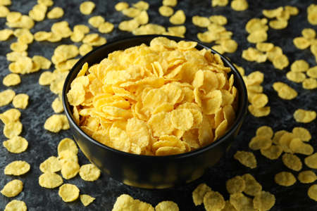 Bowl of cornflakes and sprinkled cornflakes on black smokey background