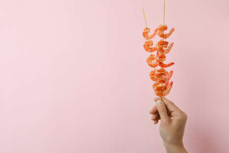 Female hand holds grilled shrimps skewers on pink backgroundの写真素材