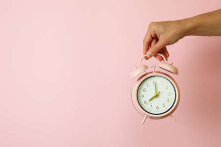 Female hand holds alarm clock on pink background
