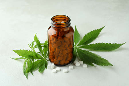 Bottle with pills and cannabis leaves on white textured backgroundの写真素材