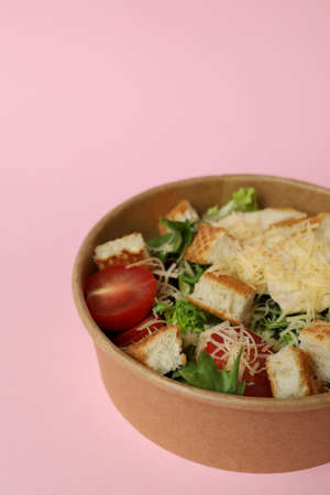 Paper bowl with Caesar salad on pink background