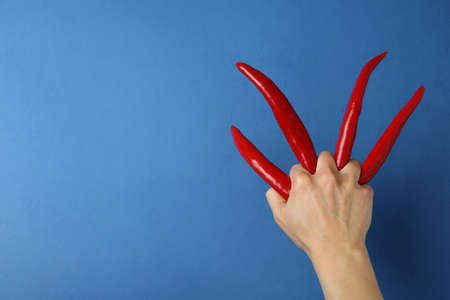 Female hand with red hot chili peppers on blue backgroundの写真素材
