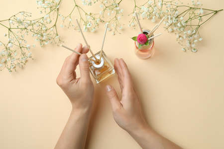 Female hands, diffusers and flowers on beige background