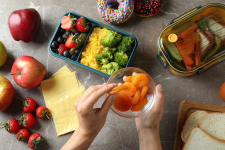 Lunch boxes with tasty food and female hands on gray textured table