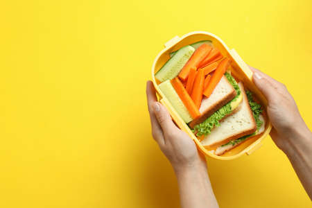Female hands hold lunch box on yellow backgroundの写真素材