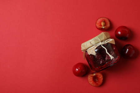 Cherry jam and ingredients on red background