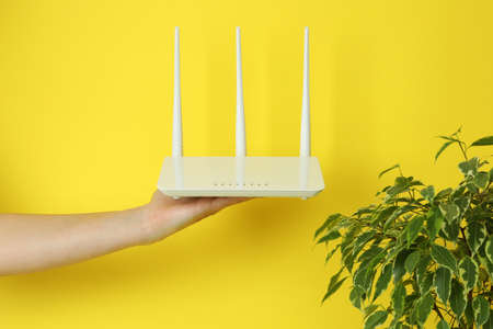 Female hand holds Wi - fi router on yellow background