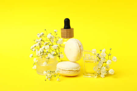 Cosmetics, macaroons and flowers on yellow background