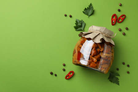 Jar with marinated mushrooms on green background