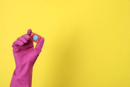 Hand in glove holds dishwashing tablet on yellow backgroundの写真素材