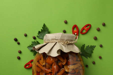 Jar with marinated mushrooms on green background