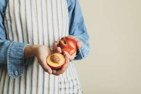 Girl in apron holds ripe peach fruitsの写真素材