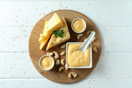 Board with cheese sauce and ingredients on white wooden tableの写真素材