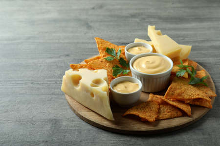 Board with cheese sauce, chips, cheese and parsley on gray textured tableの写真素材