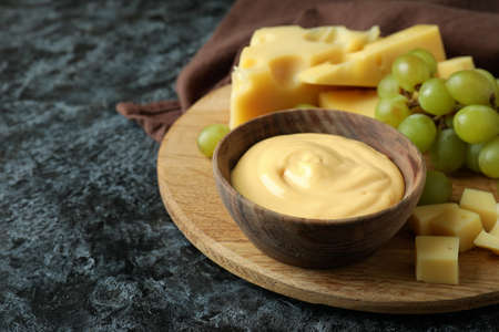 Board with cheese sauce, grape and cheese on black smokey table with kitchen towel