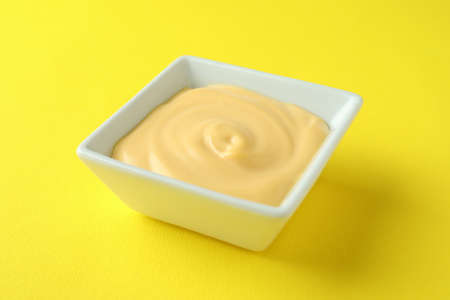 Bowl with cheese sauce on yellow backgroundの写真素材