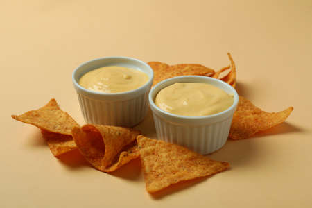 Bowls with cheese sauce and chips on beige backgroundの写真素材
