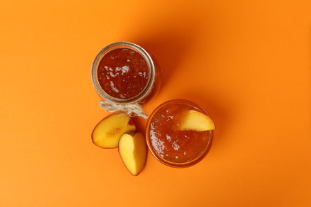 Jar and bowl of peach jam and ingredients on orange backgroundの写真素材