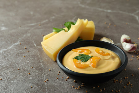 Bowl of cheese sauce and ingredients on gray textured tableの写真素材