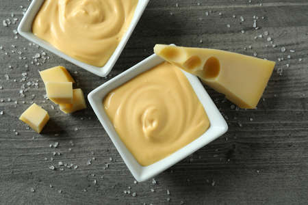 Bowls with cheese sauce, cheese and salt on gray textured table