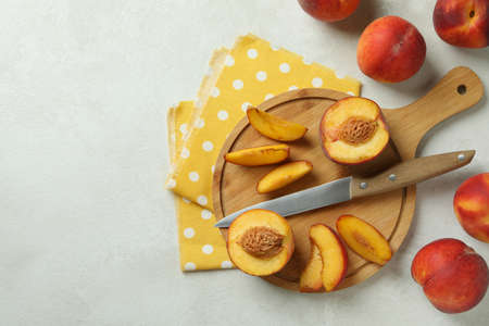 Board with peach fruits, knife and kitchen towel on white textured table